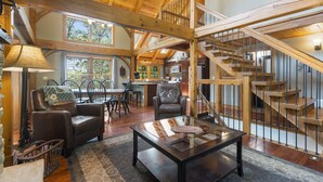 A spacious living area with a wooden staircase, leather furniture, and a view of the kitchen.