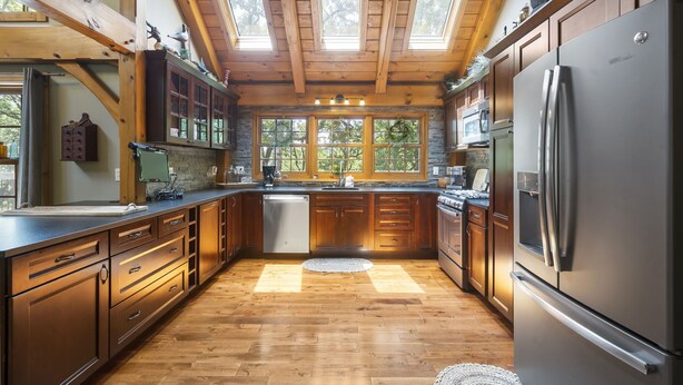 A spacious kitchen with wooden cabinets, a stainless steel refrigerator, and a large window providing natural light.