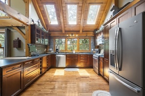 A spacious kitchen with wooden cabinets, a stainless steel refrigerator, and a large window providing natural light. - 3,000 sq ft Post & Beam Home Escape with Hot Tub, Game Room, Salt Pool & Car Charger (Blue Eye)