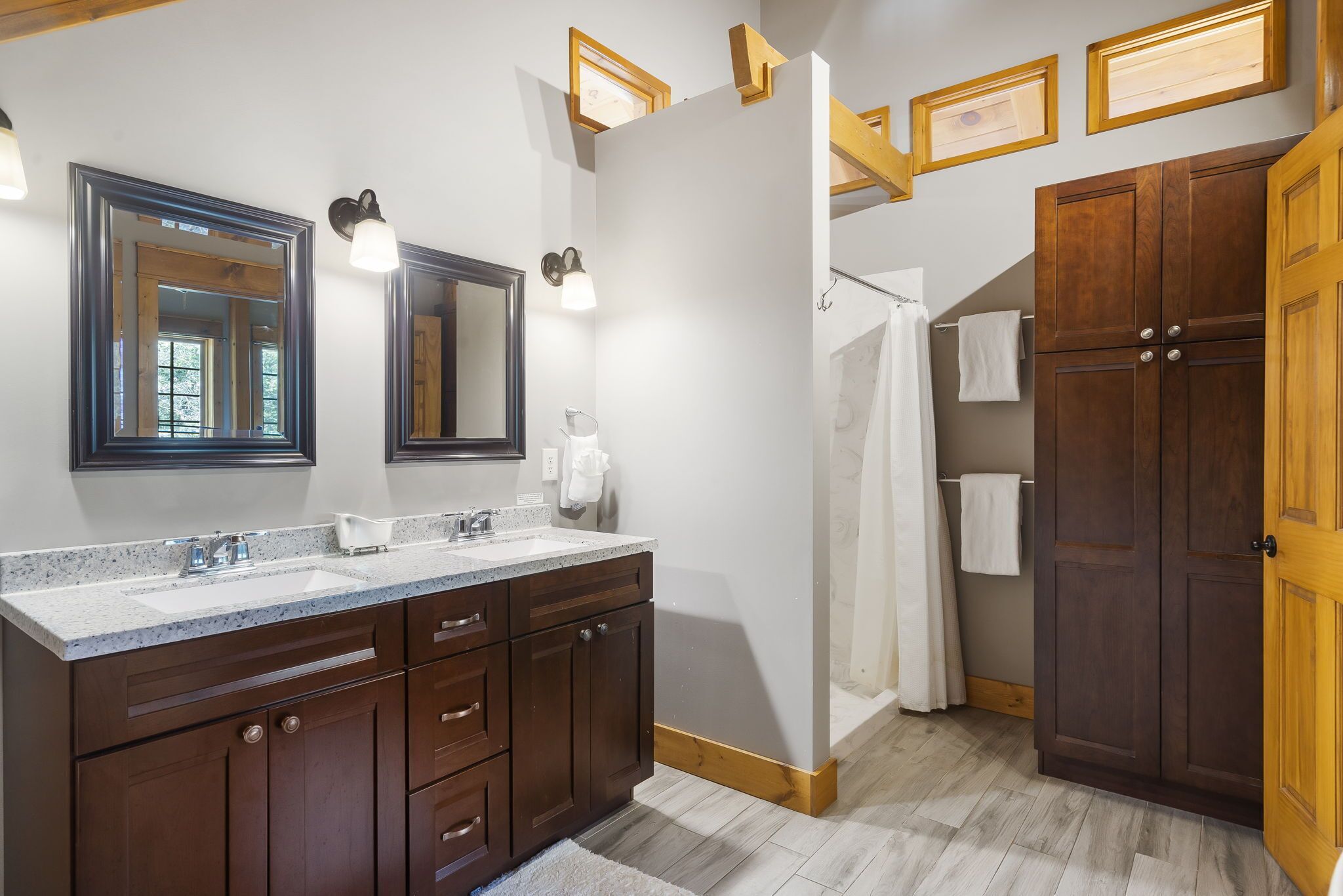 A bathroom with a double sink vanity, wooden cabinets, a large mirror, and a shower area.
