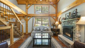 A spacious living room with a fireplace, wooden staircase, and large windows.