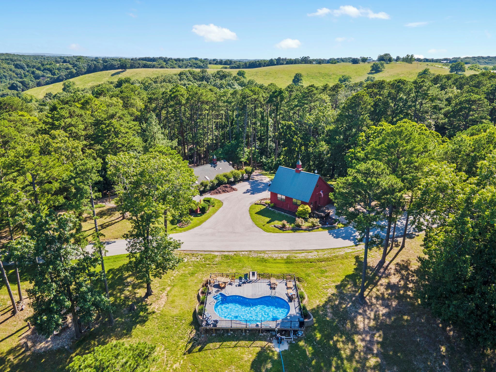 A residential property with a swimming pool, a red building, and a surrounding landscape.