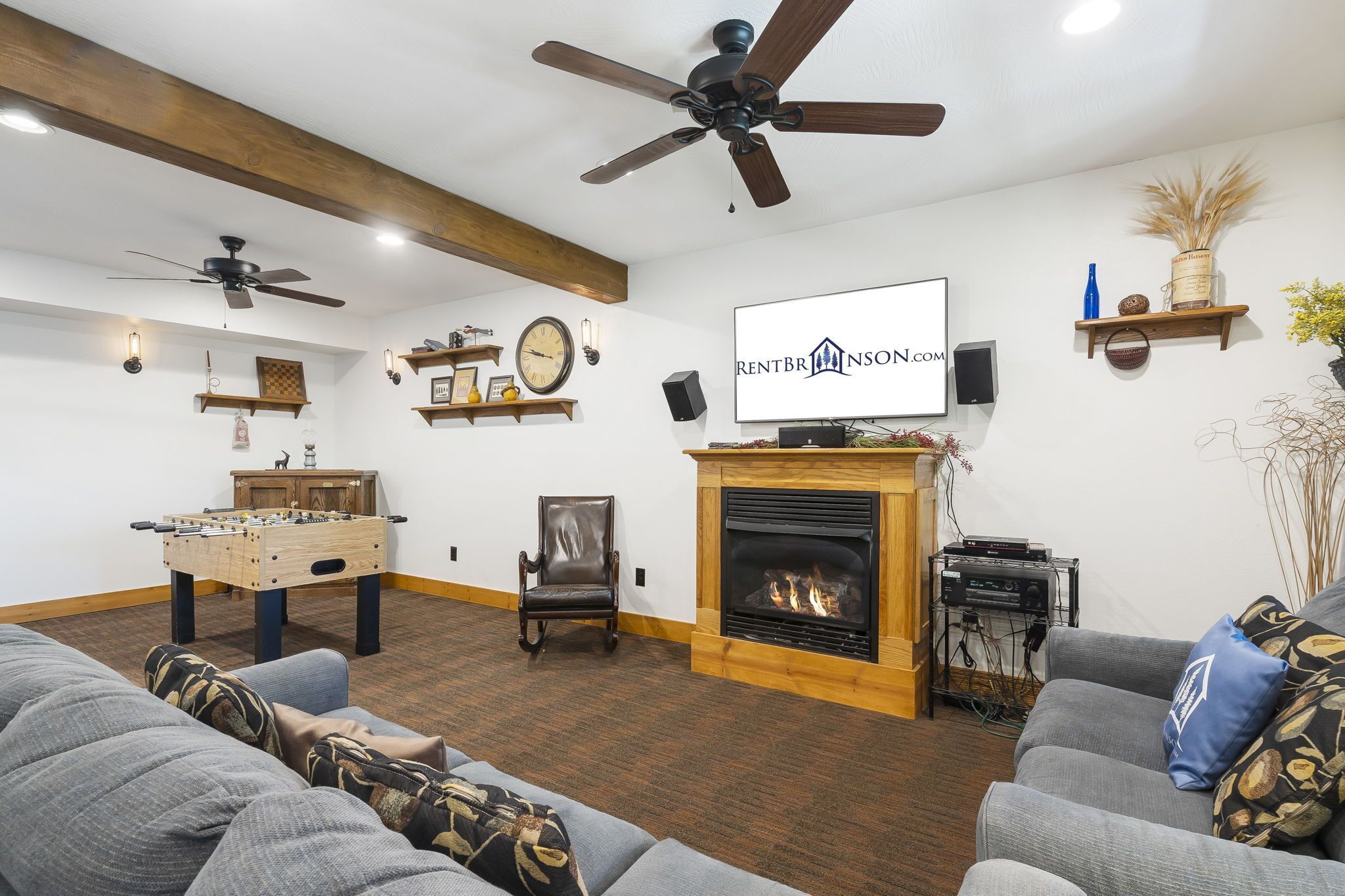 A living room with a fireplace, ceiling fans, a foosball table, and a television displaying a logo.