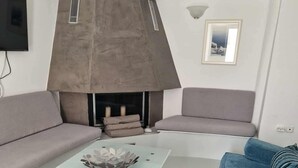En moderne stue med sofabord i glas, to sofaer, pejs og et tv ophængt på væggen.