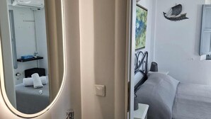Casa de banho moderna com um espelho grande, lavatório e vista para um quarto com cama e uma obra de arte na parede.