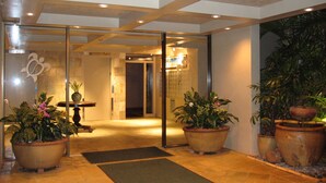 A lobby with a glass door entrance, potted plants, a reception desk, and a tiled floor. - Poipu Oceanfront, 10 steps to ocean (Poipu)