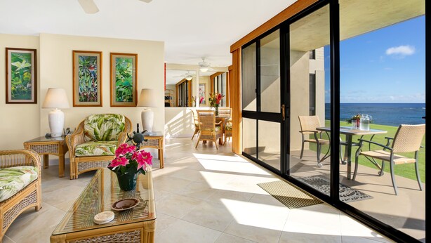 A spacious living area with wicker furniture, a glass coffee table, and artwork on the walls. - Poipu Oceanfront, 10 steps to ocean (Poipu)