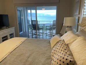 Quarto de hotel com cama, televisão, varanda com cadeiras e vista para o mar.