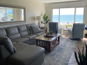A living room with a sofa, a coffee table, and a chair. There is a view of the ocean through large windows. - STAR property-Direct Ocean 2 BDRM 5th FL Corner Condo-Pool-Near KSC Space Center (Cocoa Beach)