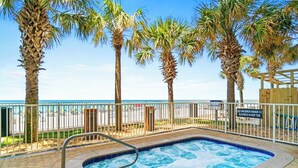 A hot tub area with a pool, surrounded by palm trees and a beach view.