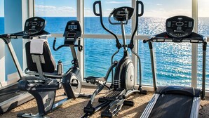 A gym with cardio machines and a treadmill, overlooking a scenic ocean view.