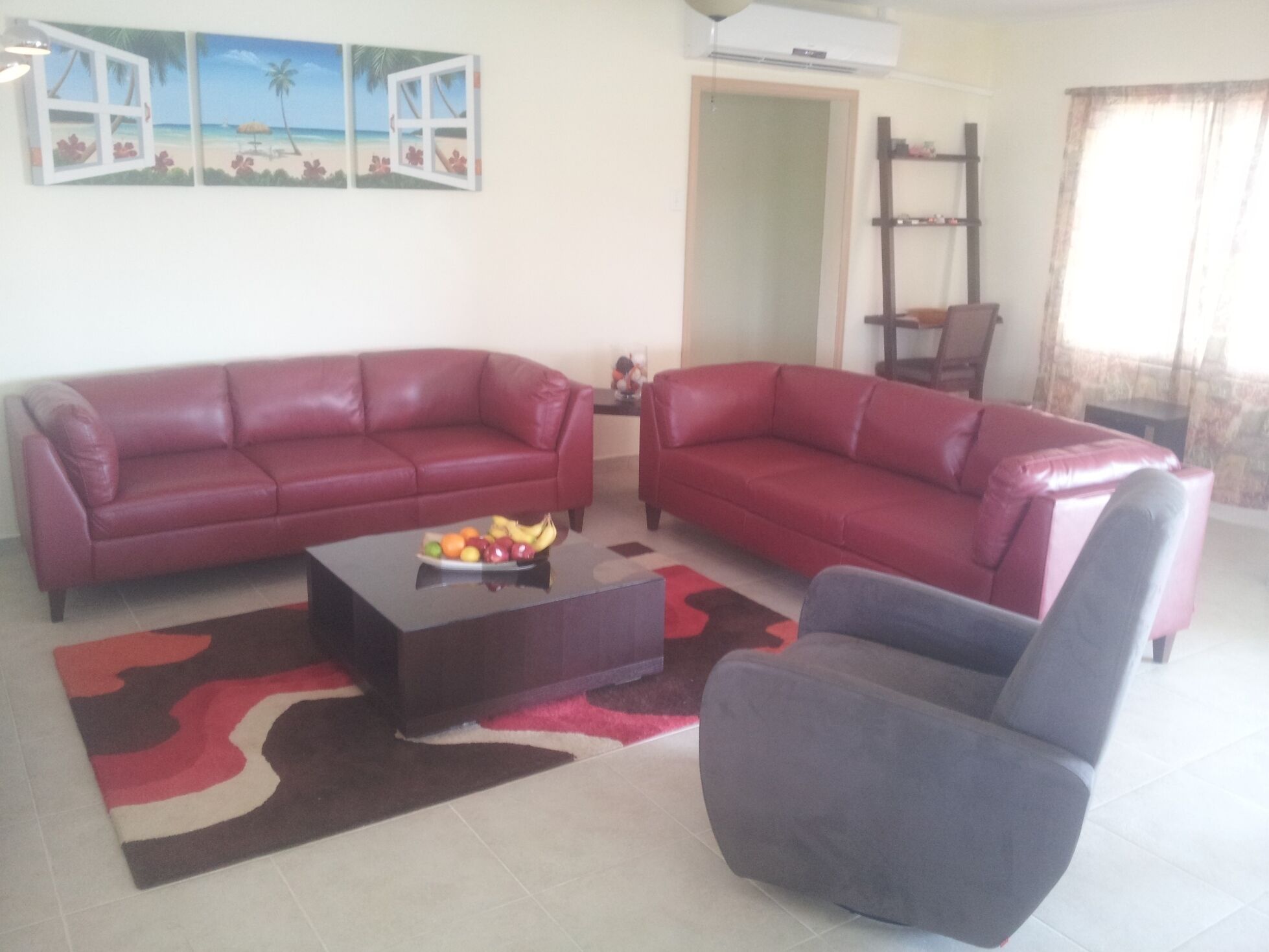A living room with two red sofas, a coffee table with fruit, and a grey armchair.