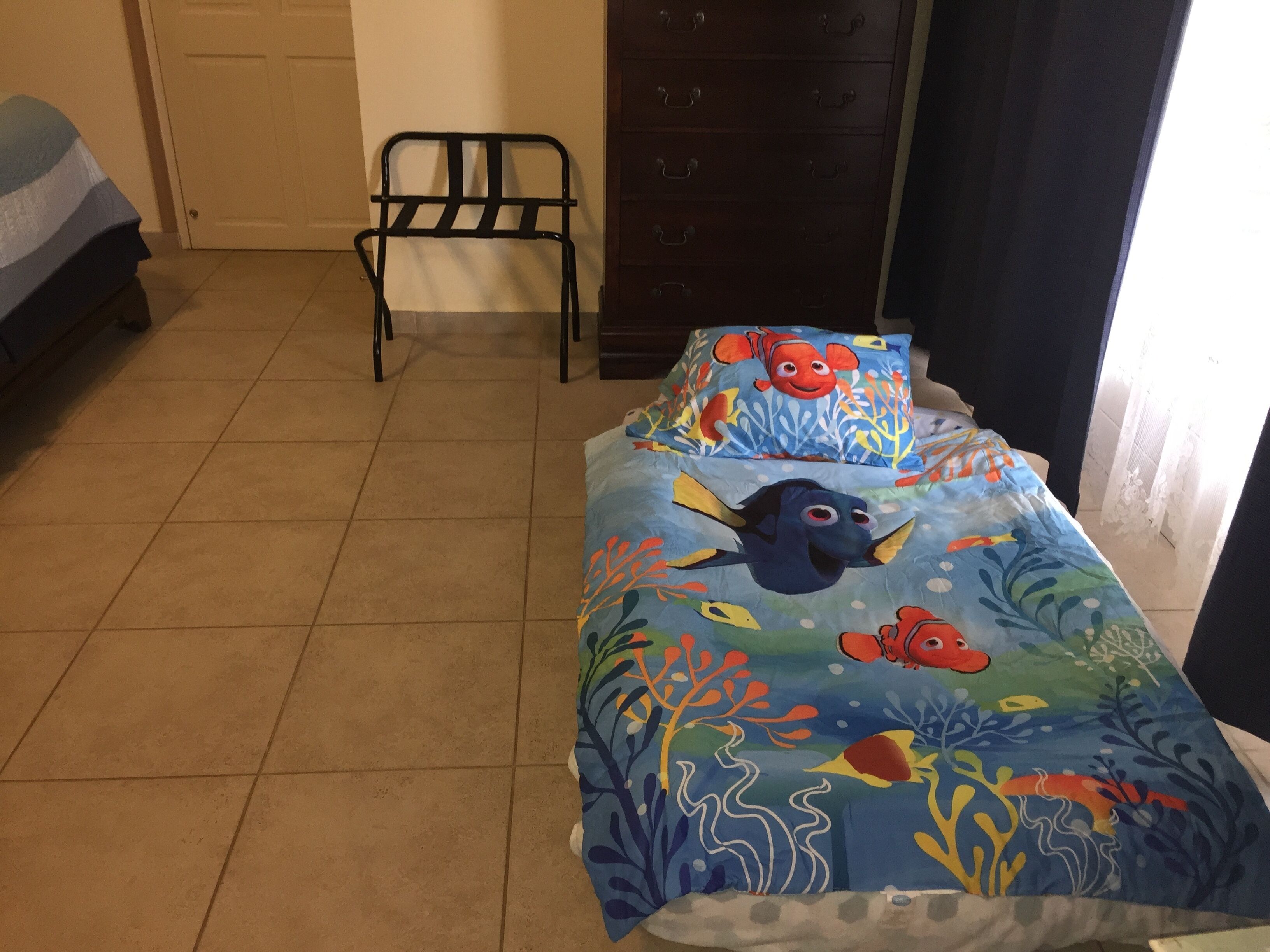 A bedroom with a bed featuring a colorful underwater-themed bedspread, a chair, and a dresser.
