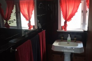 Un baño con un lavamanos blanco, cortinas rojas y una bañera negra.