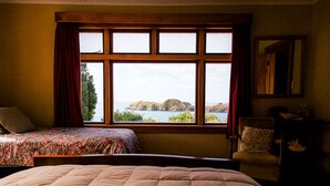 Ein Schlafzimmer mit einem großen Bett, einem kleineren Bett, einem Fenster mit Meerblick und einem Sessel.