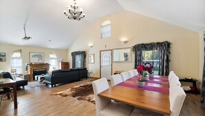 A spacious living area with a fireplace, a dining table with chairs, and a large window with curtains.