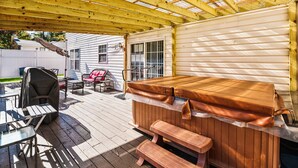 A covered outdoor deck with a hot tub, wooden benches, and a grill.