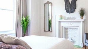 Ein Schlafzimmer mit einem Bett, einem Spiegel, einem Kamin und Dekorationselementen.