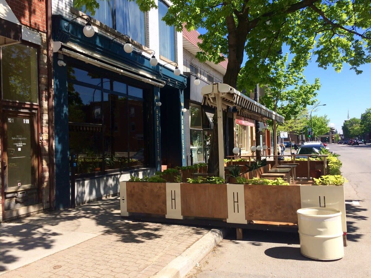 Vista de una calle con un restaurante que ofrece mesas al aire libre, un toldo azul y una señalización con la dirección claramente visible.