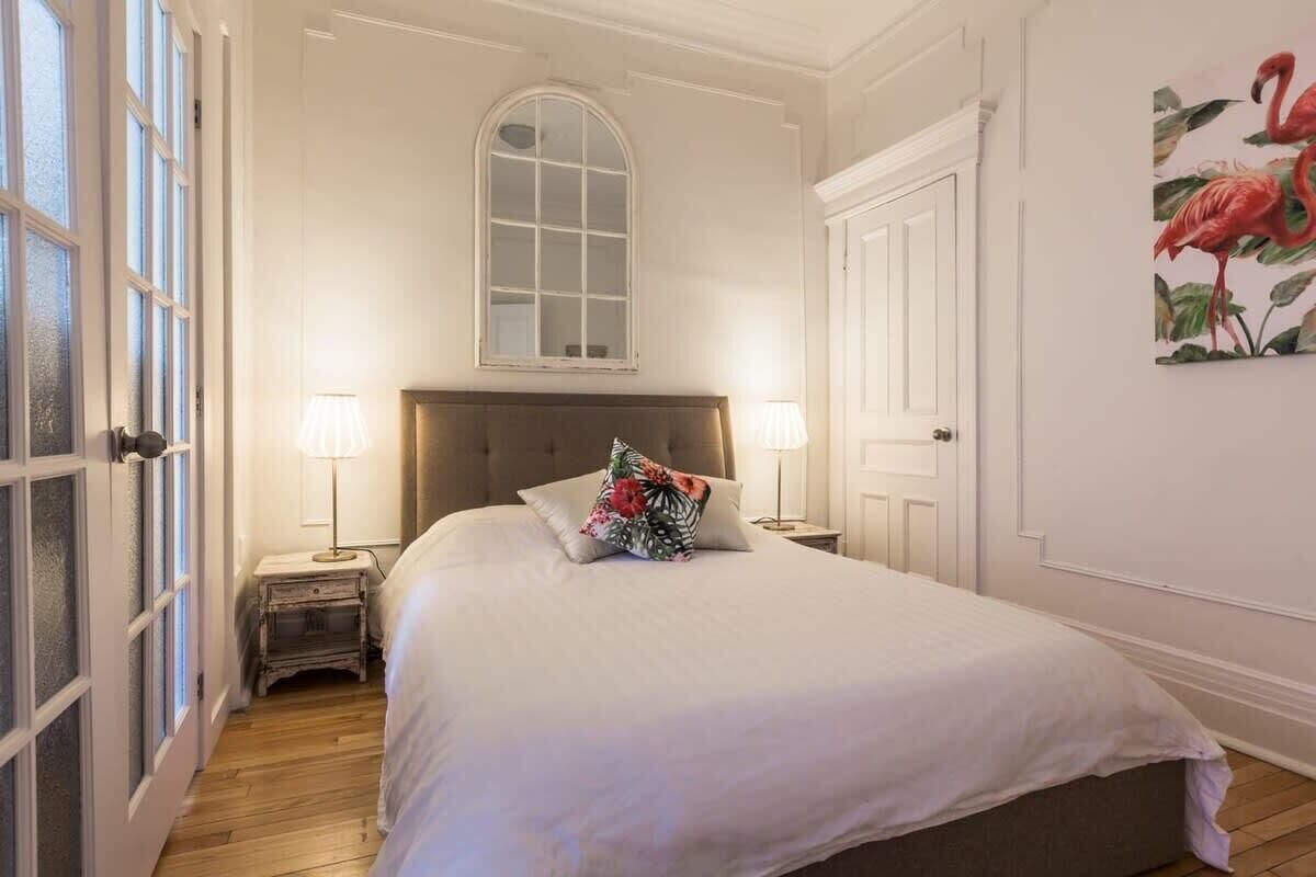 Une chambre à coucher avec un grand lit, deux lampes de chevet, une table de nuit, une fenêtre donnant sur un beau paysage et une porte.