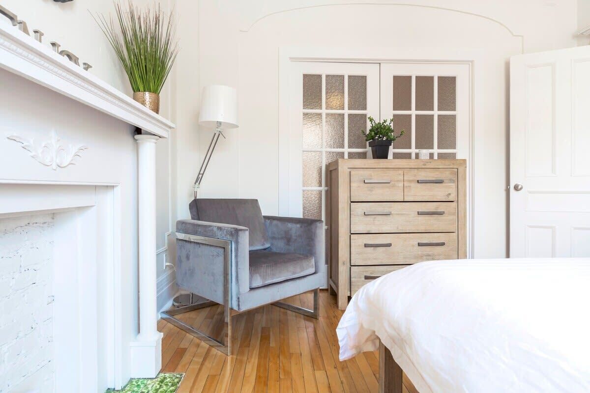 A bedroom with a bed, a grey armchair, a wooden dresser, and a white door with frosted glass panels.
