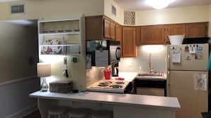 A kitchen with wooden cabinets, a white countertop, a stove, and a refrigerator. - Oceanfront! Topsail Dunes Beachfront Condo with Pool and Balcony (North Topsail Beach)
