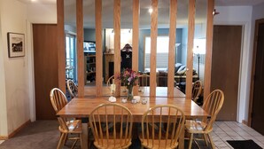 Une salle à manger avec une table et des chaises en bois, un vase rempli de fleurs et un téléviseur en arrière-plan.