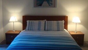 A bedroom with a bed, two bedside tables, and a painting on the wall. - Beach Place-family friendly (Lakes Entrance)