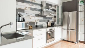 A modern kitchen with a stainless steel refrigerator, a built-in oven, and a large island with a sink. - MTLVR #15 | Plateau gem, patio, Metro 3 min (Montreal)
