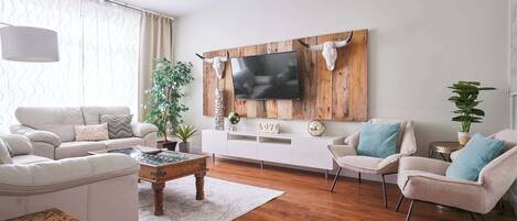 Una sala de estar moderna con un mueble bajo para el televisor de madera, sofás blancos y una mesa de centro.