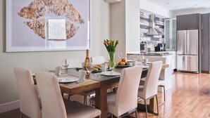 A modern dining area with a wooden table and white chairs, a large abstract painting on the wall, and a kitchen in the background. - MTLVR #15 | Plateau gem, patio, Metro 3 min (Montreal)