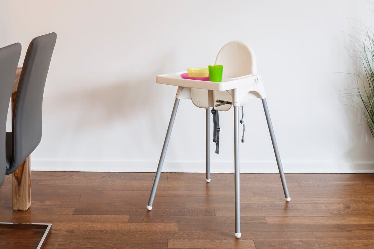 Una silla alta con mesita, ubicada en una habitación con suelo de madera y pared blanca.