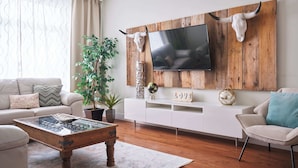 A living room with a wooden TV wall mount, a sofa, a coffee table, and a potted plant. - MTLVR #15 | Plateau gem, patio, Metro 3 min (Montreal)