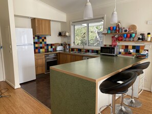 A modern kitchen with wooden cabinets, a central island with bar stools, a colorful backsplash, and a window providing natural light. - Dog friendly close to beach/shops, trampoline, hot outside shower, NBN Wifi (Sandy Point)