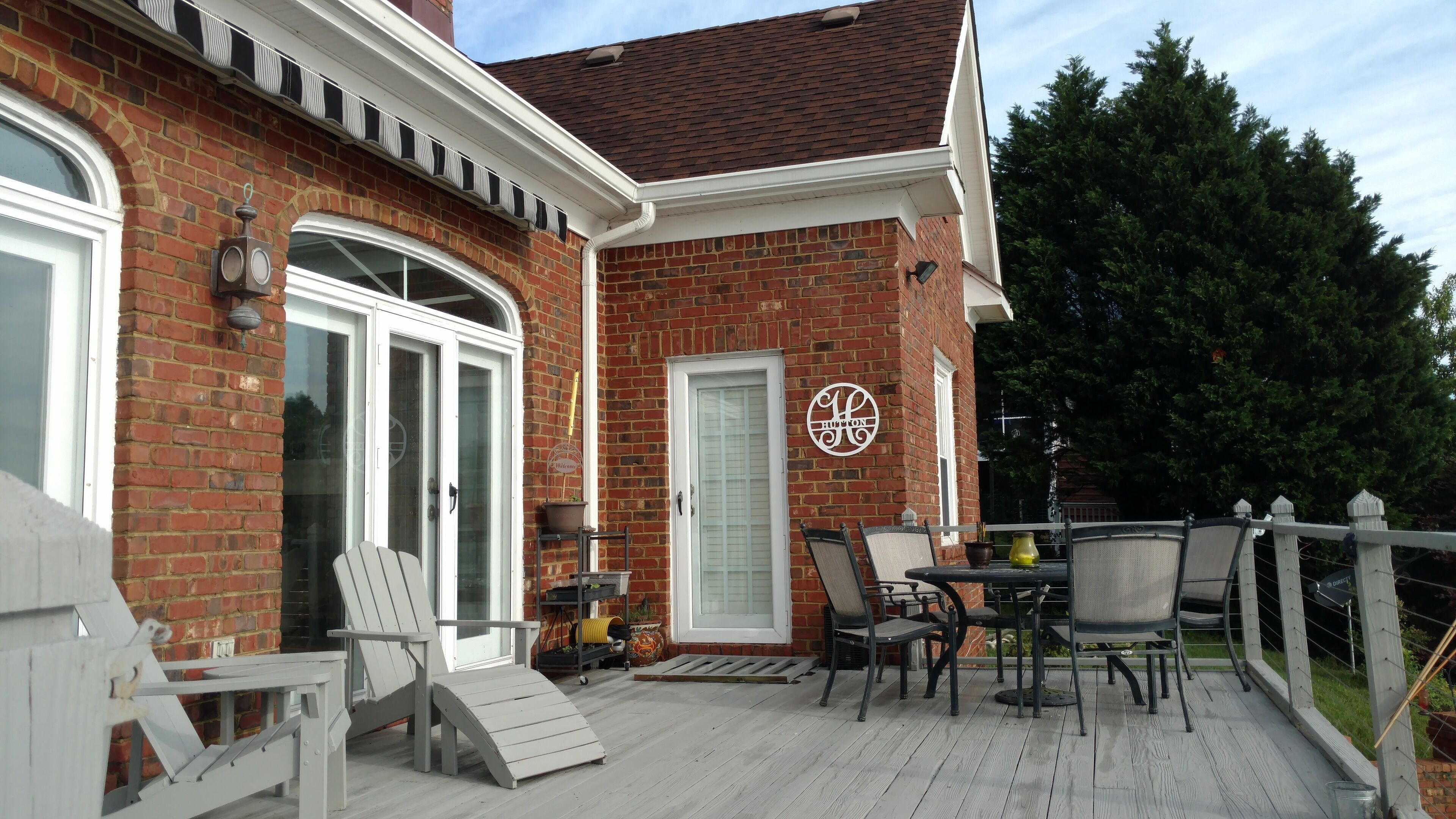 A brick house with a deck, a dining table with chairs, and a door with a sign.