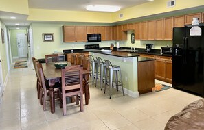 A kitchen with wooden cabinets, a black refrigerator, and a dining area with wooden chairs and a table.