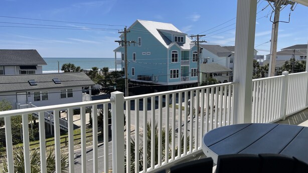 A balcony with a view of a blue house, a street, and the ocean. - Bubbles Up. Ocean View Corner Unit in Coconut Grove. North Myrtle Beach, SC (North Myrtle Beach)
