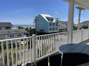 A balcony with a view of a blue house, a street, and the ocean. - Bubbles Up. Ocean View Corner Unit in Coconut Grove. North Myrtle Beach, SC (North Myrtle Beach)