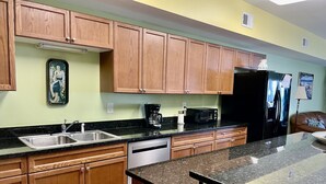 A kitchen with wooden cabinets, a stainless steel sink, a dishwasher, a microwave, and a refrigerator. - Bubbles Up. Ocean View Corner Unit in Coconut Grove. North Myrtle Beach, SC (North Myrtle Beach)