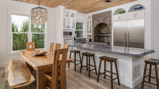 Une cuisine moderne avec un plafond en bois, des meubles blancs, un îlot central doté de tabourets de bar et un grand réfrigérateur.