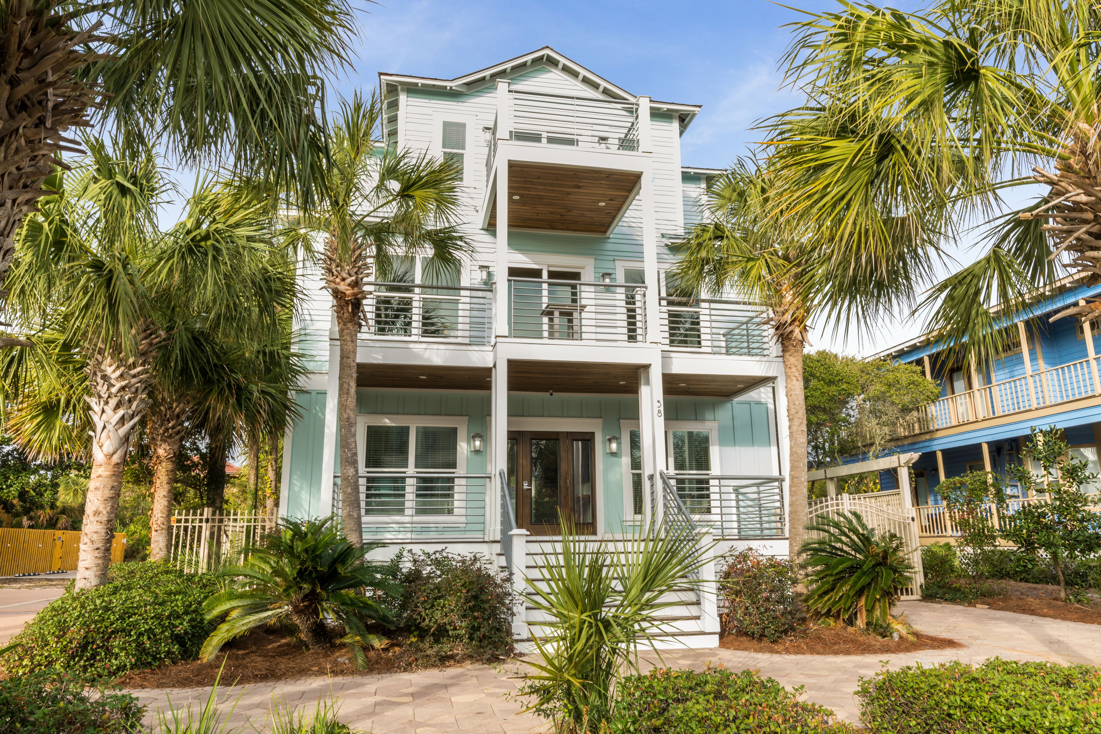 A two-story building with a balcony, surrounded by palm trees and shrubs.