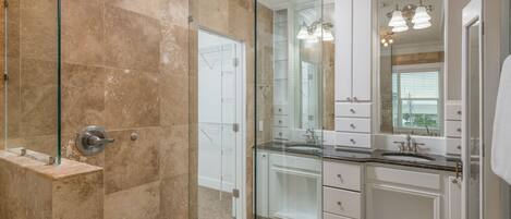 A modern bathroom with a glass-enclosed shower, white cabinetry, and a large mirror.