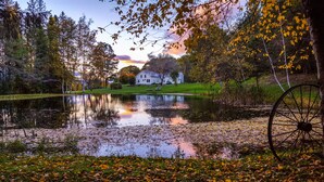 A serene lakeside scene with a house and a large wheel in the foreground.