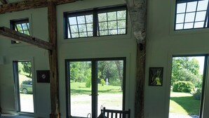 A spacious room with a large wooden table, benches, and large windows offering views of a green landscape.
