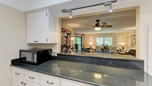 A kitchen with a microwave, granite countertop, white cabinets, and a ceiling fan.