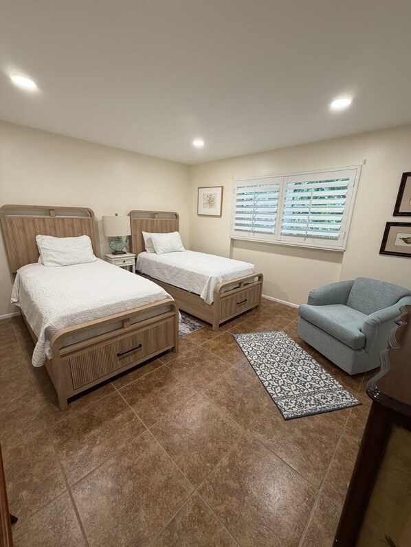 A bedroom with two beds, a sofa, a window with blinds, and a rug.