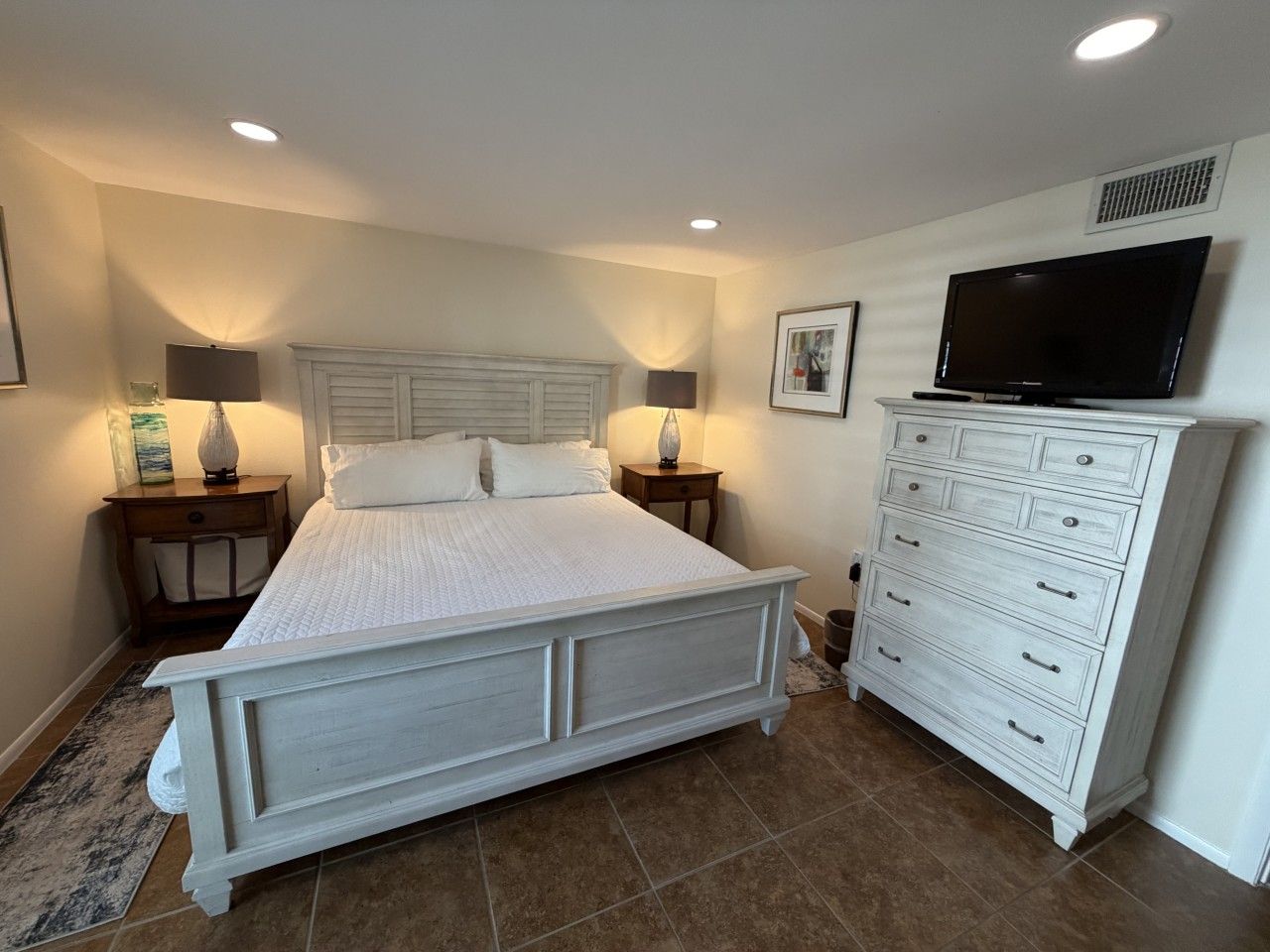 Une chambre à coucher avec un grand lit, deux tables de chevet, une commode et un téléviseur fixé au mur.