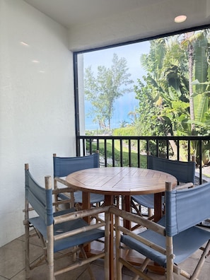 A round wooden table with six chairs, a balcony with a view of greenery and a building, and a white wall. - Sea Grape Inn #4- Beachfront Property (Longboat Key)
