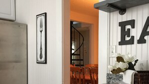 Una cucina con mobili bianchi, un piano di lavoro in granito e un'area pranzo con una scala.