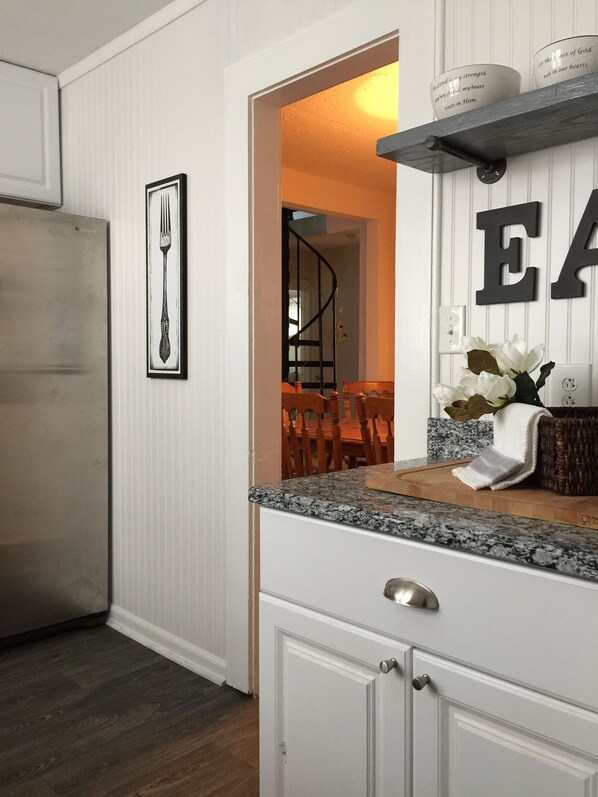 A kitchen with white cabinetry, a granite countertop, and a dining area with a staircase.
